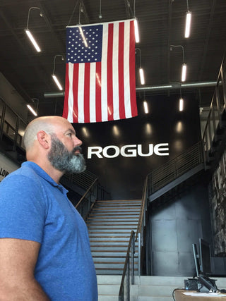 Mark Harris standing in the Rogue Fitness Lobby with an American Flag hanging down from the ceiling.