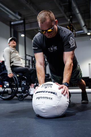 A Visually Impaired Man on his knees and leaning on an Equip - Dynamax White Wall ball in a gym