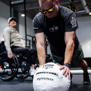 A Visually Impaired Man on his knees and leaning on an Equip - Dynamax White Wall ball in a gym