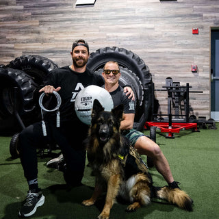 A Visually impaired man and his seeing eye dog holding white gym equipment such as a wall ball