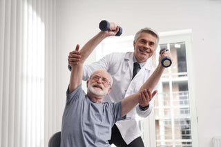 Elderly man with dumb bells high in the air with a doctor behind him holding with his hands on the mans elbows to assure he doesn't drop them.