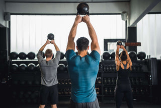 Three people using kettle bells in a gym setting looking away from the camera