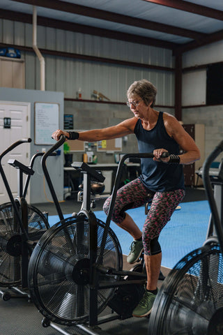 A Lady in her seventies using an Assault Bike in a gym setting