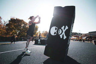 Amy Bream Pushing "The Coffin" tire flip device outdoors at the 2022 WheelWOD Games with the sun behind her.