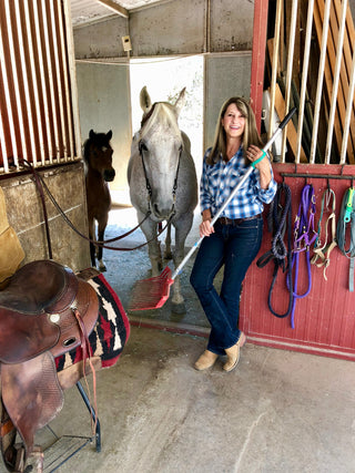 Woman standing with a horse in a stable holding a muck rake