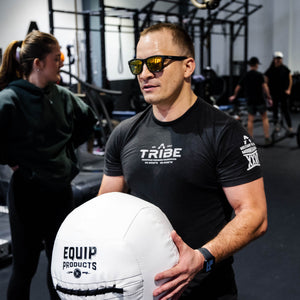 A Visually Impaired Man holding an Equip - Dynamax White Wall ball in the seated position and in a gym setting.