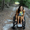 Liz Mozingo in her wheelchair on a gravel path with trees overhanging and appears to have rained recently. she is kind of dipping down to the camera and smiling really cute