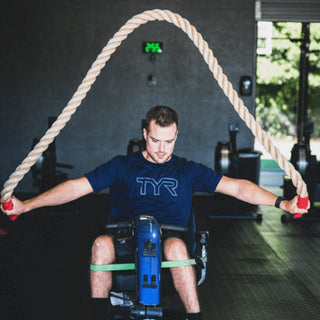 A Man in a wheelchair swinging a large 2" Monster rope over his back 