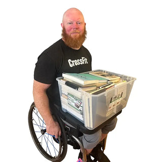 Man in a wheelchair holding a large storage bin filled with books and papers, using a HandyMat