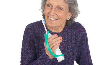 EazyHold Teacher & Therapist 7-Pack cuff grip aid used by an elderly woman for holding a toothbrush.
