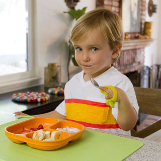 Child using EazyHold Teacher & Therapist 7-Pack universal cuff grip aid with a plate of fruit.