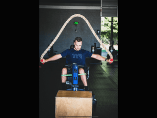 A Man in a wheelchair swinging a large 2" Monster rope over his heard back and forth from front to back.