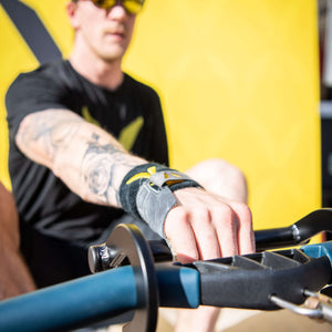 Black aluminum rowing hook on a concept2 rower handle with athlete rowing with one hand wearing black shirt and hat with a yellow event background