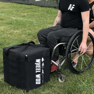 Wheelchair Athlete Josh young in a wheelchair about to pickup a square cushioned box made with black denier material and weighted for workouts called The Package.